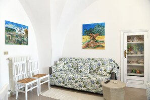 A room with a white sofa, two white chairs, a wicker ottoman, a white radiator, and a door with a glass panel. - Agata's House nel fascino del Borgo (Cisternino)