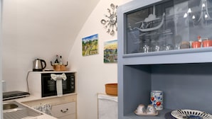 Cozinha compacta com pia, fogão e micro-ondas. Há objetos decorativos na parede e um armário com copos.