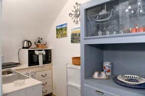 Eine kleine Küche mit Spüle, Herd und Mikrowelle. An der Wand sind dekorative Elemente und ein Schrank mit Gläsern.