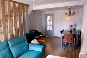 En stue med blå sofa, træafskærmning, sort sofa, spisebord med stole og en lysekrone.