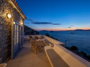 A stone building with a terrace overlooking the sea, featuring outdoor seating and a view of distant islands. - Hydrelion Beachfront Suite, Divine Sea Views, Furnished Terrace, Hydra (Hydra)