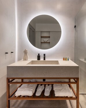 A modern bathroom with a round mirror, a sink, and a wooden shelf with towels. - Hydrelion Beachfront Suite, Divine Sea Views, Furnished Terrace, Hydra (Hydra)