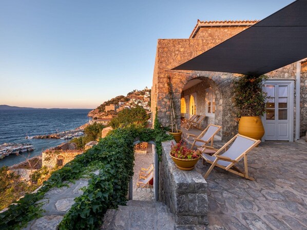 A stone building with a terrace overlooking the sea, featuring a large potted plant and wooden lounge chairs. - Beachfront Villa Ondyrelis, Divine Sea Views, Furnished Terrace, Hydra (Hydra)
