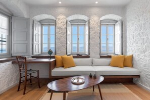 A room with a white stone wall, a wooden desk, a white sofa with yellow cushions, and a wooden chair. - Beachfront Villa Ondyrelis, Divine Sea Views, Furnished Terrace, Hydra (Hydra)