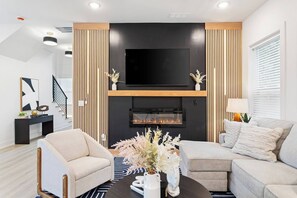 A modern living room with a fireplace, two sofas, a coffee table, and a TV mounted above the fireplace. - Sleek Designer Retreat Near Downtown Atlanta (Atlanta)