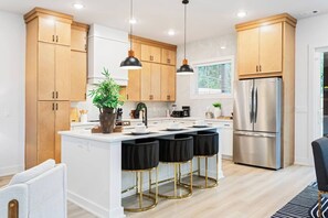 A modern kitchen with wooden cabinets, a stainless steel refrigerator, a central island with stools, pendant lighting, and a potted plant. - Sleek Designer Retreat Near Downtown Atlanta (Atlanta)