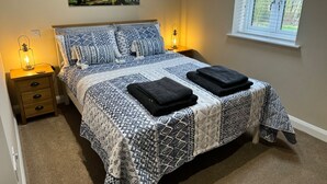 Une chambre à coucher comprenant un lit, deux tables de chevet, une commode, une fenêtre avec des stores et une décoration murale sur le thème de la forêt.