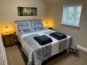 Ein Schlafzimmer mit einem Bett, zwei Nachttischen, einem Fenster mit Jalousien und Wandbildern zum Thema Wald.