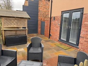 Eine Terrasse mit Korbmöbeln, einem hölzernen Spielhaus und einer Ziegelmauer mit einer Schiebetür.