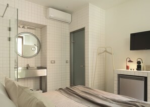 A hotel room with a bed, a bedside table, a mirror, a wall-mounted air conditioner, a door, a TV, and a small heater.