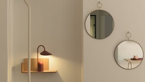 En minimalistisk væg med en hylde, hvorpå der står en lampe og to vægmonterede spejle.