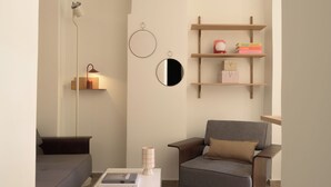 En moderne stue med sofa, lænestol, sofabord, vægmonterede hylder og en lampe.
