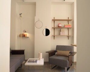 A modern living room with a sofa, armchair, coffee table, wall-mounted shelves, and a lamp.
