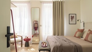 Un dormitorio con una cama, una silla, un espejo, una mesita con una bandeja y una puerta que da a otra habitación.
