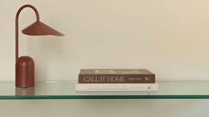Una lámpara de escritorio, un libro titulado 'Call It Home' de Amber Lewis, y un espejo sobre una repisa de vidrio.