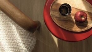 Una mesa de madera con un borde rojo, un cuenco de madera, una taza de metal y una manzana roja.