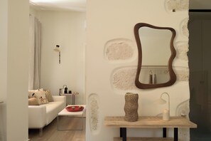 Ett modernt vardagsrum med en vit soffa, ett litet bord, en spegel och en lampa.