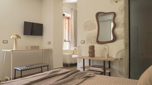 A bedroom with a bed, a bench, a desk, a chair, a mirror, and a television. - Two Bedroom Suite with Balcony, Spartacus Garden (Rethymno)