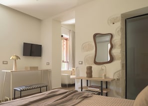 Une chambre à coucher comprenant un lit, un banc, un bureau, une chaise, un miroir et un téléviseur.