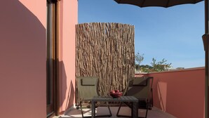 A balcony with a woven bamboo screen, two chairs, a small table, and a potted plant. - Two Bedroom Suite with Balcony, Spartacus Garden (Rethymno)
