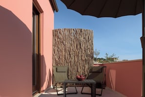 Un balcon agrémenté d’un paravent en bambou tressé, de deux chaises, d’une petite table et d’une plante en pot.