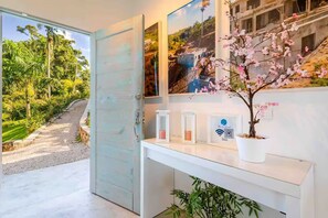 Eine moderne Hotelrezeption mit Glastür zu einem Garten, einem weißen Konsolentisch mit gerahmten Bildern und einem QR-Code für den WLAN-Zugang.