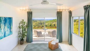 A bedroom with a large bed, a potted plant, a painting, and a balcony with a view.
