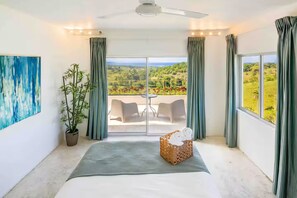 Ein Schlafzimmer mit einem großen Bett, einer Zimmerpflanze, einem Gemälde und einem Balkon mit Blick.
