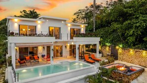 A modern two-story house with a swimming pool, outdoor seating, and a stone wall.