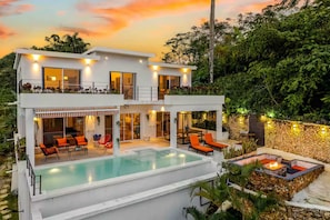 Ein modernes, zweistöckiges Haus mit Swimmingpool, Sitzgelegenheiten im Freien und einer Steinsäule.