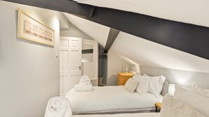 Ein Schlafzimmer mit schrägen Wänden, einem Bett mit weißer Bettwäsche, einem Nachttisch mit Lampe und einem gerahmten Bild an der Wand.