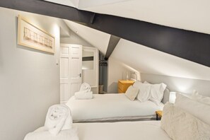 Ein Schlafzimmer mit schrägen Wänden, einem Bett mit weißer Bettwäsche, einem Nachttisch mit Lampe und einem gerahmten Bild an der Wand.