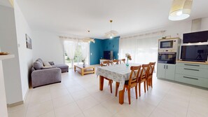 Ein modernes Wohnzimmer mit einer Couch, einem Esstisch mit Stühlen, einem Fernseher und einer Küchenzeile mit Schränken und Geräten.