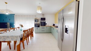A modern kitchen with a dining area, featuring a large refrigerator, a microwave, and a dining table with chairs. - Serenity – Family home with a garden and Wi-Fi in (Saint-Jean-de-Monts)