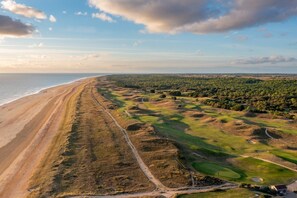 Eine Vogelperspektive eines Küsten-Golfplatzes mit Strand, grünen Fairways und einer entfernten Küstenlinie.