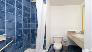 Un bagno con piastrelle blu, una vasca da bagno bianca, un water e un lavabo con piano in color crema.