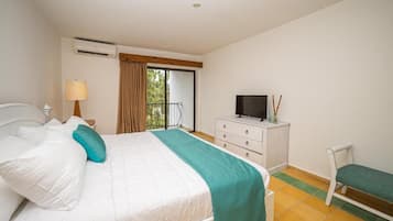 Un dormitorio con cama, televisor, cómoda, silla y ventana con cortinas.