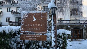 A sign for 'APARTUR CATEDRAL' with a snow-covered environment and a stone building in the background. - Apartur Catedral (San Carlos de Bariloche)