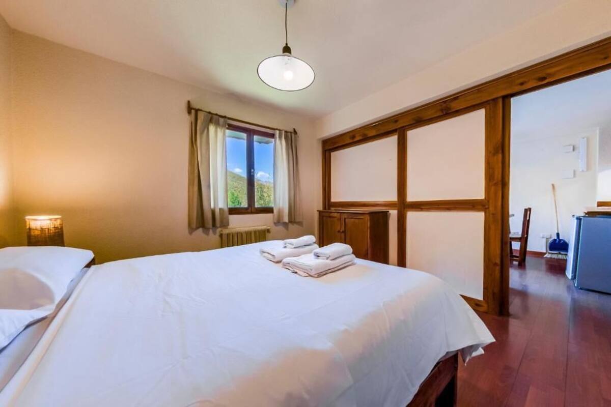 Habitación de hotel con dos camas, una ventana con cortinas, una puerta de madera y un escritorio con una silla.
