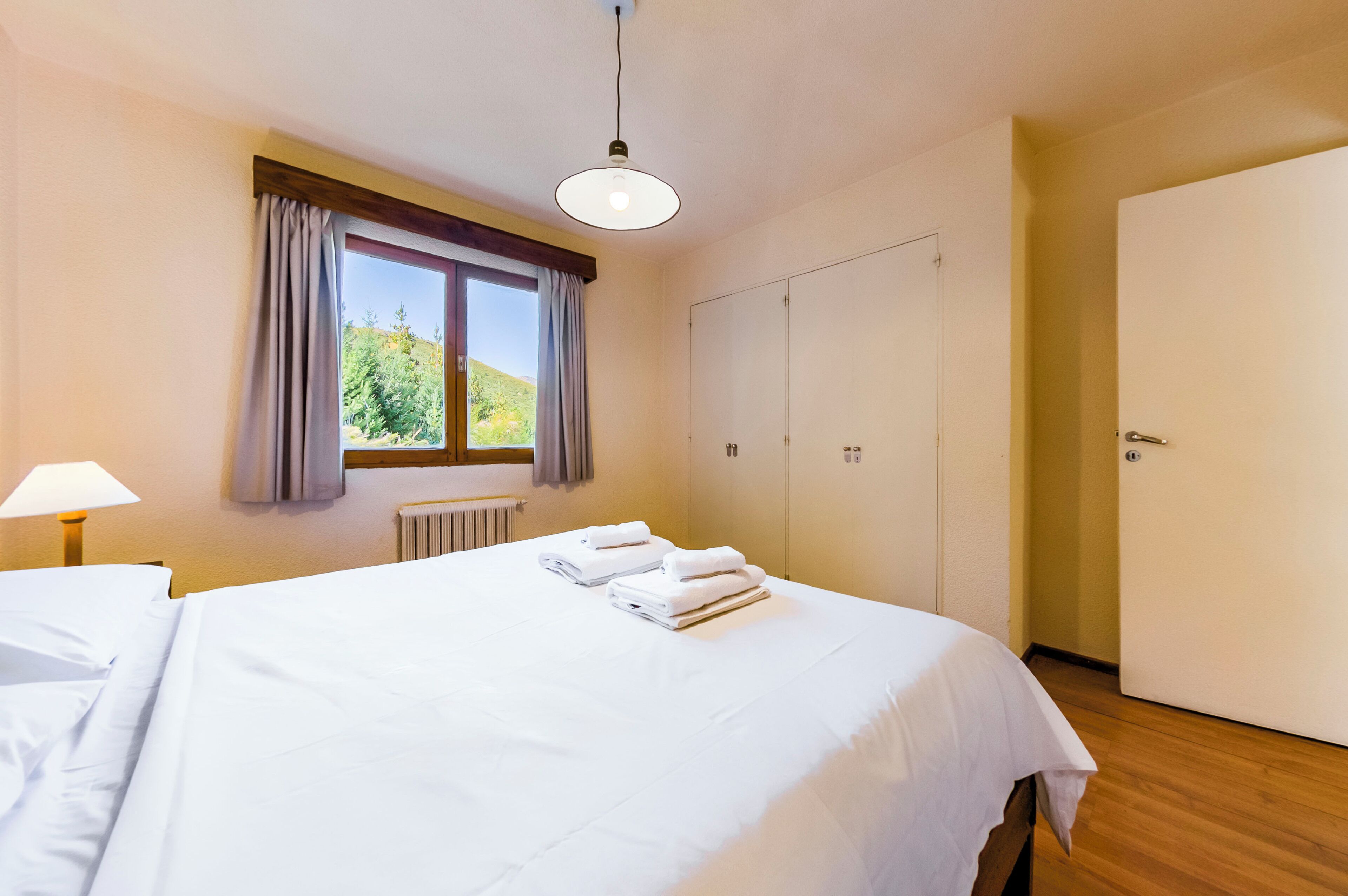 Hotellihuone, jossa on sänky, ikkuna verhoineen, vaatekaappi ja lamppu.