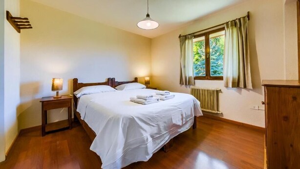 A bedroom with a bed, bedside lamps, a window with curtains, and a radiator. - Apartur Catedral (San Carlos de Bariloche)