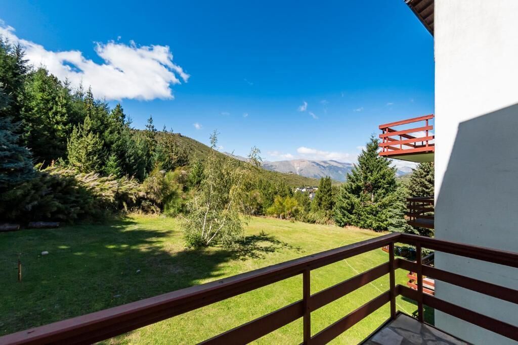 Un balcón con vista a un área verde, árboles y montañas a lo lejos.