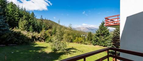 Un balcón con vista a un área verde, árboles y montañas a lo lejos.