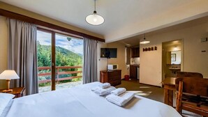 A hotel room with a large bed, a desk, a chair, a TV, and a balcony with a view of greenery. - Apartur Catedral (San Carlos de Bariloche)