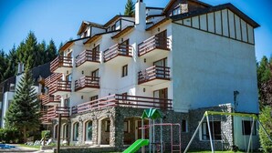 A multi-story building with balconies, a playground, and a stone facade. - Apartur Catedral (San Carlos de Bariloche)