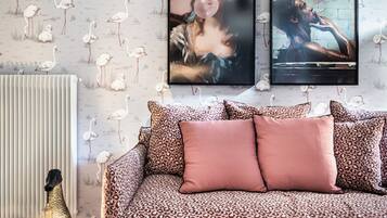 Une pièce avec un papier peint à motifs, un canapé à imprimé léopard, un pouf rose et un radiateur.