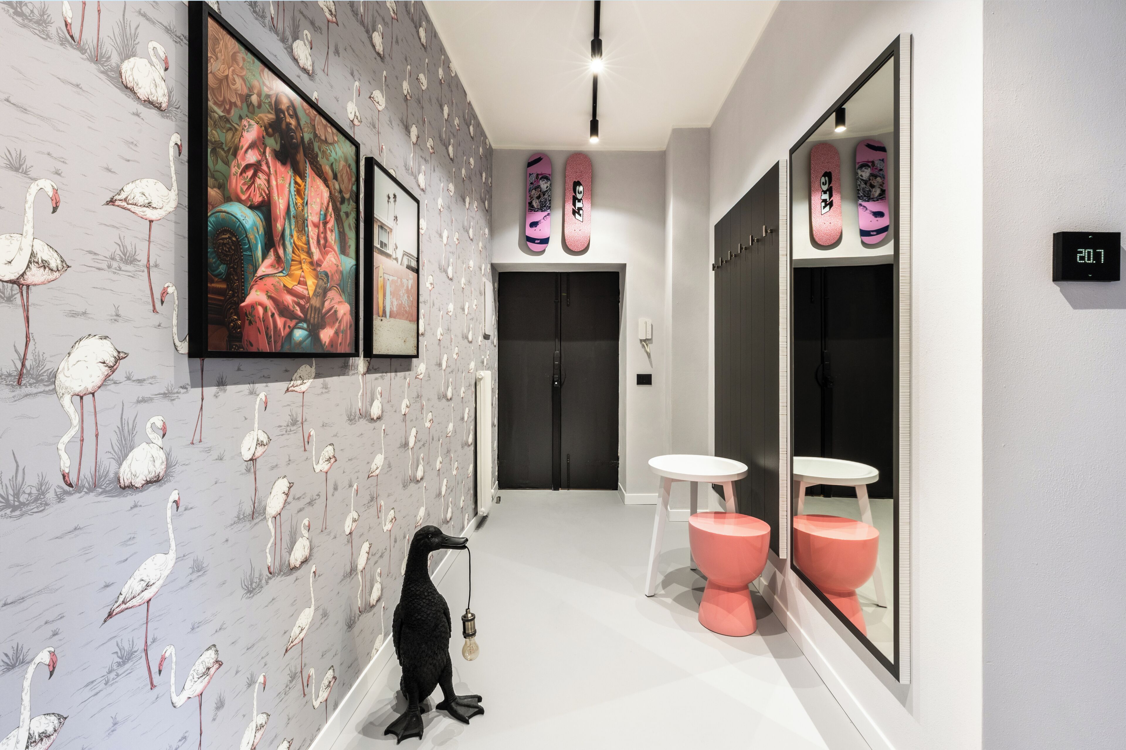 A hallway with a wall mural of flamingos, a black sculpture, and a digital clock displaying 20:07.