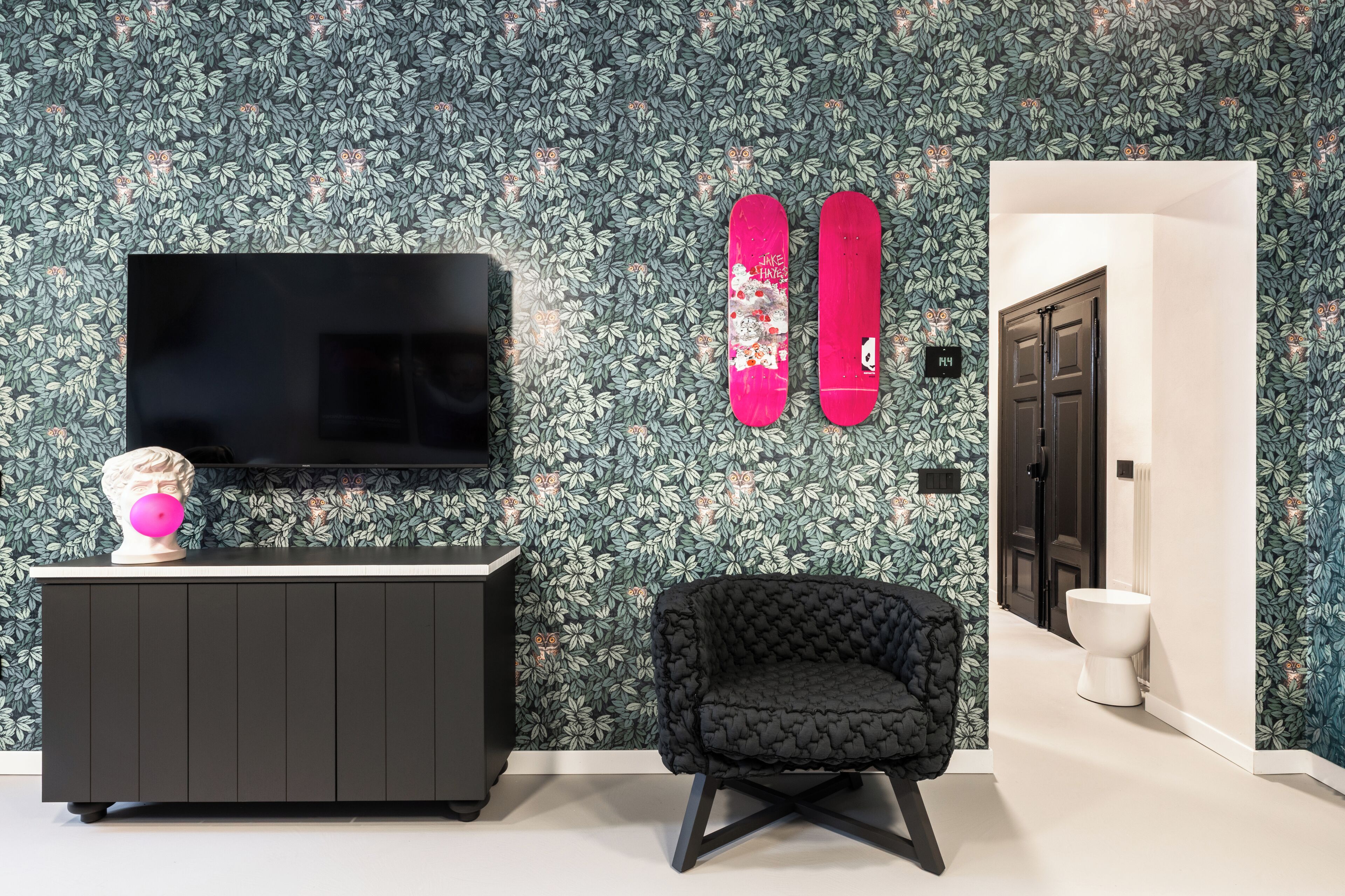 Un salón moderno con un televisor de pantalla plana grande, un sillón tapizado negro, un busto decorativo y un papel tapiz estampado.