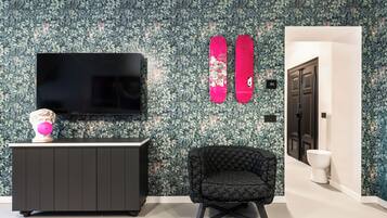 Un salón moderno con un televisor de pantalla plana grande, un sillón tapizado negro, un busto decorativo y un papel tapiz estampado.