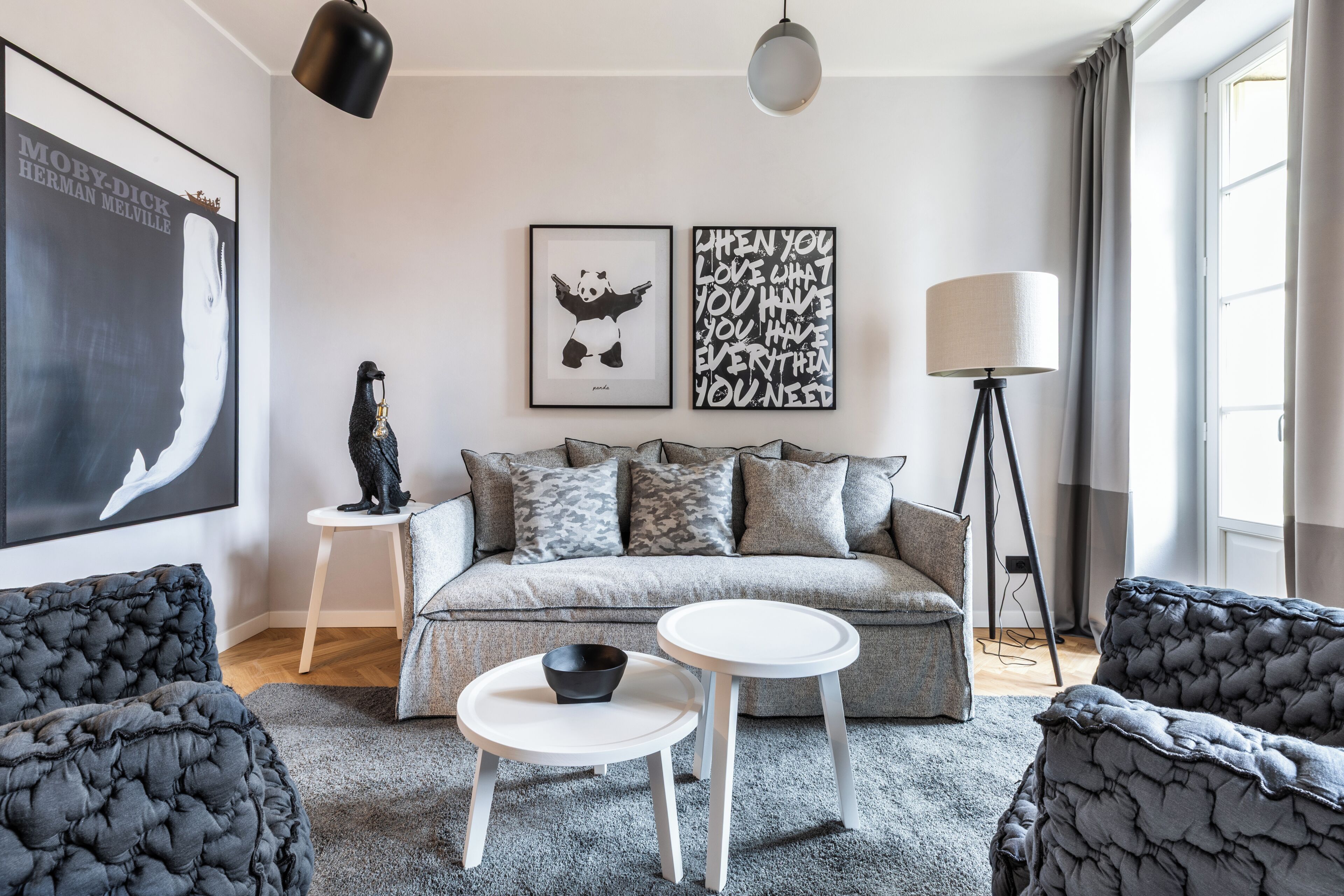 A modern living room with a grey sofa, two white side tables, a black floor lamp, and artwork on the walls.